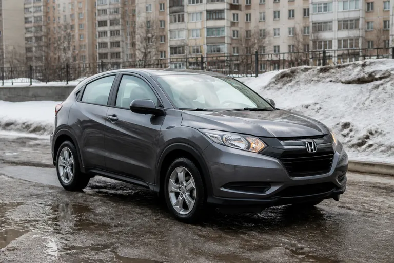 Honda HR-V стоит на городской дороге в северном российском городе зимой. На фоне видны многоэтажные дома, влажный асфальт и мягкий дневной свет.