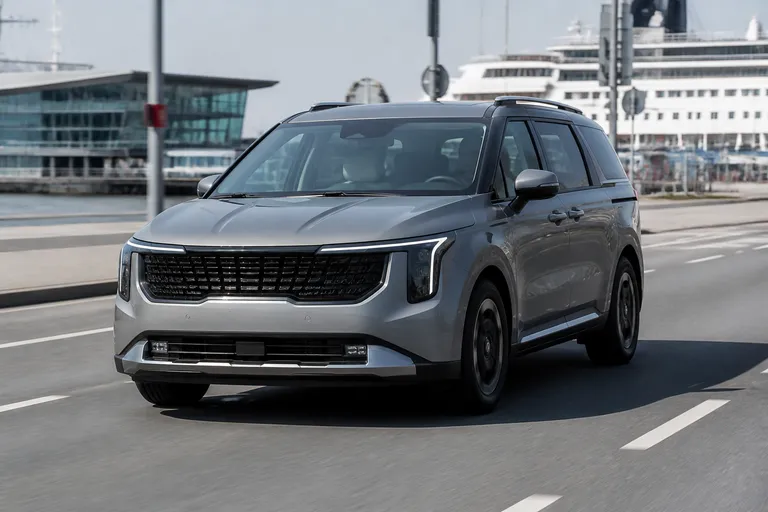Kia Carnival на городской дороге, рядом виден современный портовый терминал. Сцена передаёт тему покупки и доставки автомобиля из Кореи.