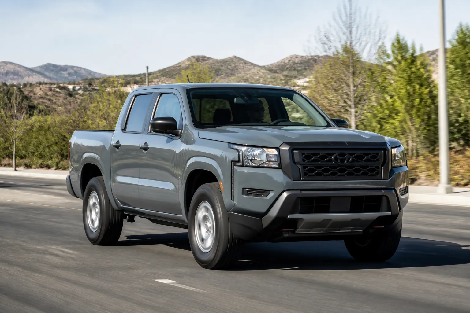 Новый пикап Nissan Frontier на городской дороге с горным пейзажем на заднем плане. Автомобиль снят в реалистичном ракурсе спереди сбоку при дневном свете.