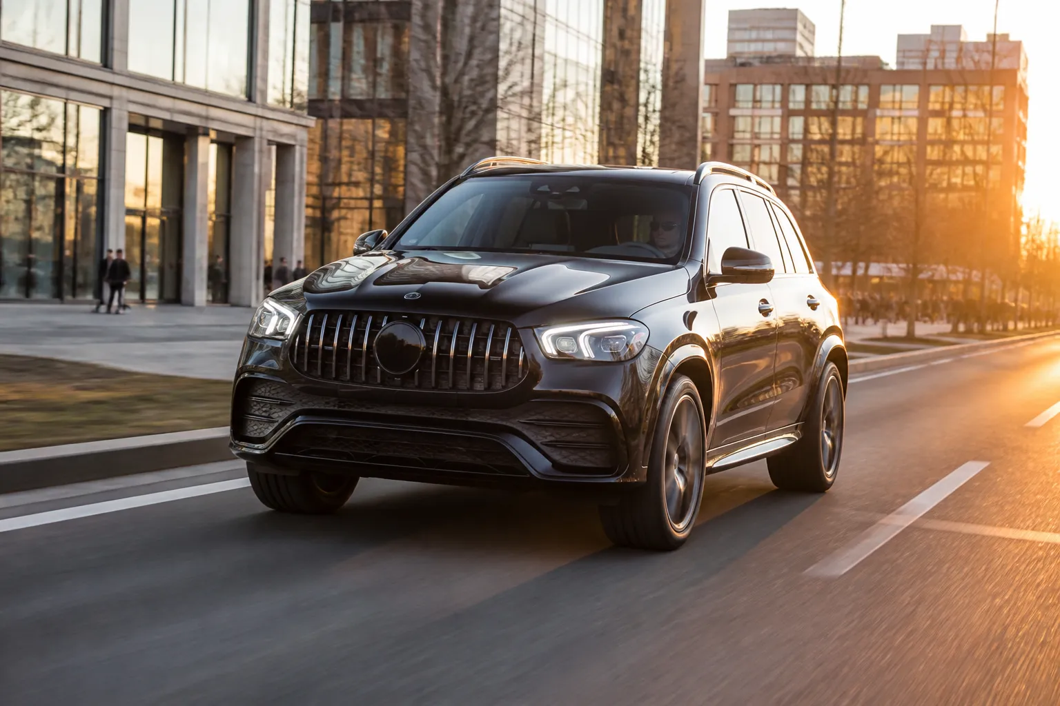 Новый Mercedes-Benz GLE на городской дороге в вечернем свете. Автомобиль показан спереди сбоку на фоне современной городской застройки.