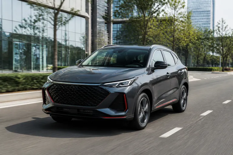 Новый Changan X5 Plus на городской дороге перед современными зданиями. Автомобиль снят спереди под углом в естественном дневном свете.
