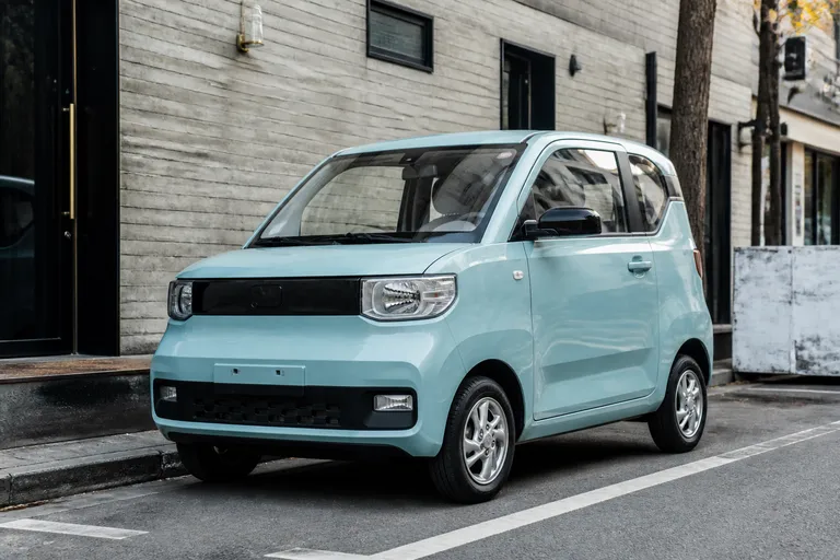 Компактный Wuling Hongguang Mini EV стоит на городской улице рядом с современными зданиями. Машина показана как небольшой электромобиль для повседневных поездок по городу.