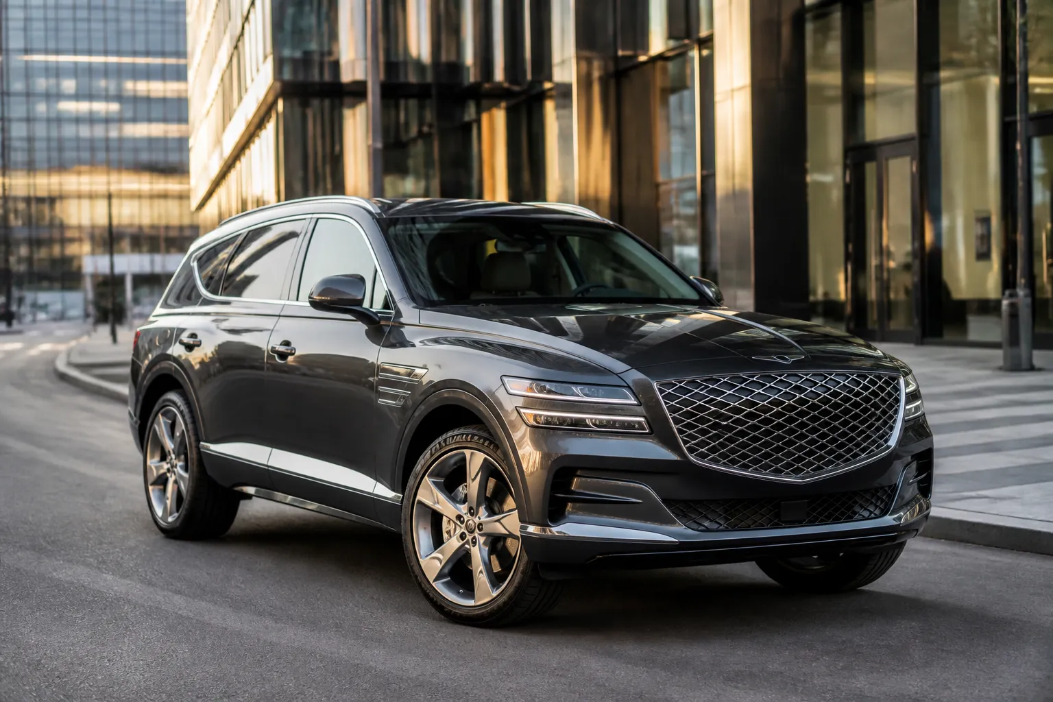 Genesis GV80 стоит на городской улице перед современной архитектурой. Вид спереди под углом подчёркивает крупный кузов и премиальный характер кроссовера.