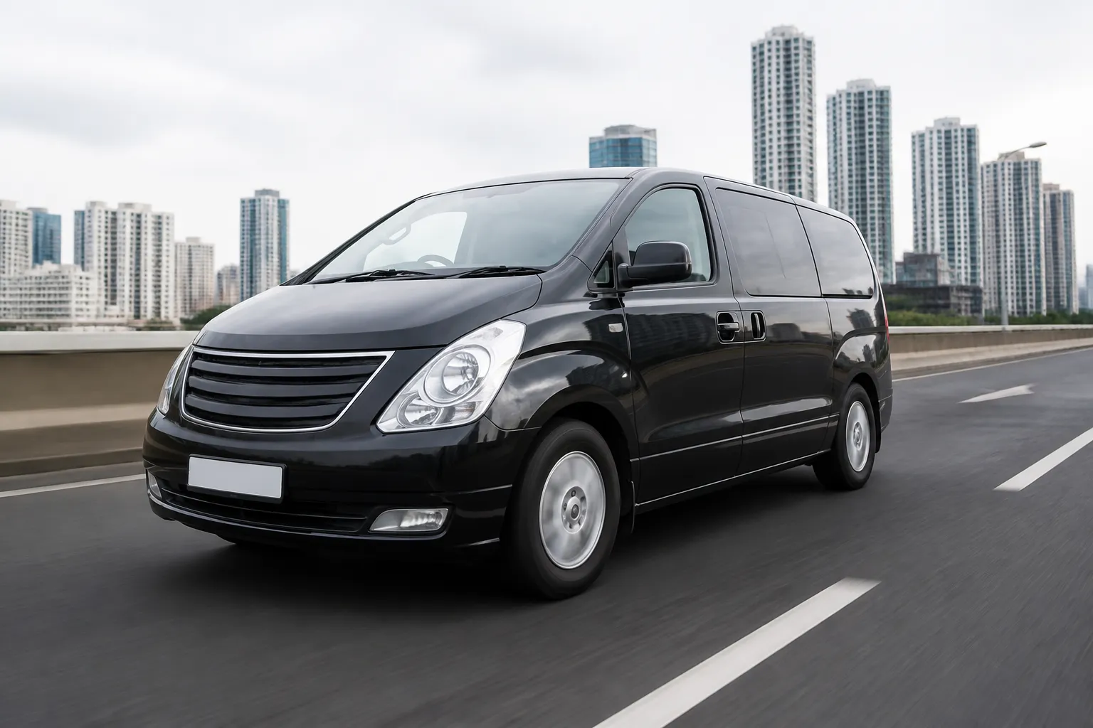 Hyundai Starex на городской дороге, снятый спереди сбоку в естественном дневном свете. На фоне видны улица и припаркованные автомобили.