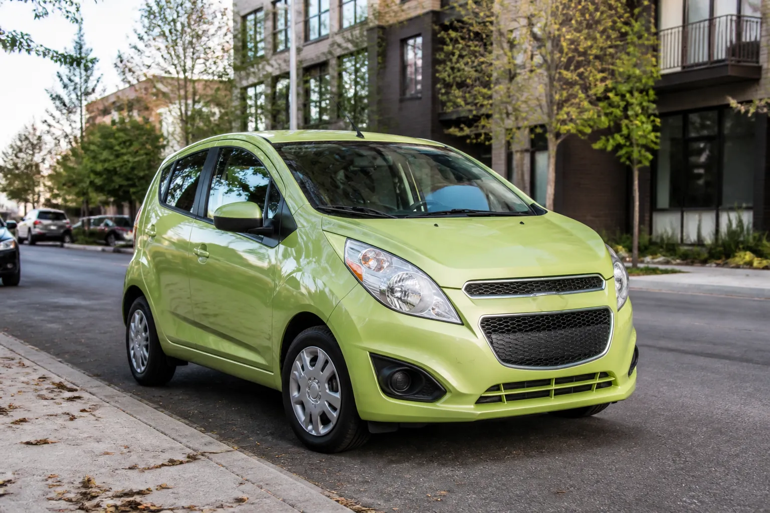 Компактный Chevrolet Spark на городской улице у парковки. Машина показана в естественном дневном свете, акцент на небольшие габариты и городскую эксплуатацию.