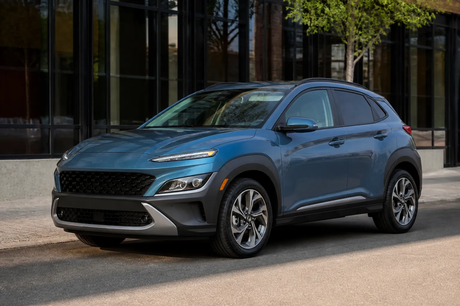Hyundai Kona на городской улице перед осмотром перед покупкой. Автомобиль стоит у обочины в дневном свете, рядом виден спокойный городской трафик.