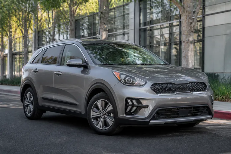 Kia Niro на городской улице перед выездом на осмотр автомобиля. На фоне видны современные дома и мягкий дневной свет.