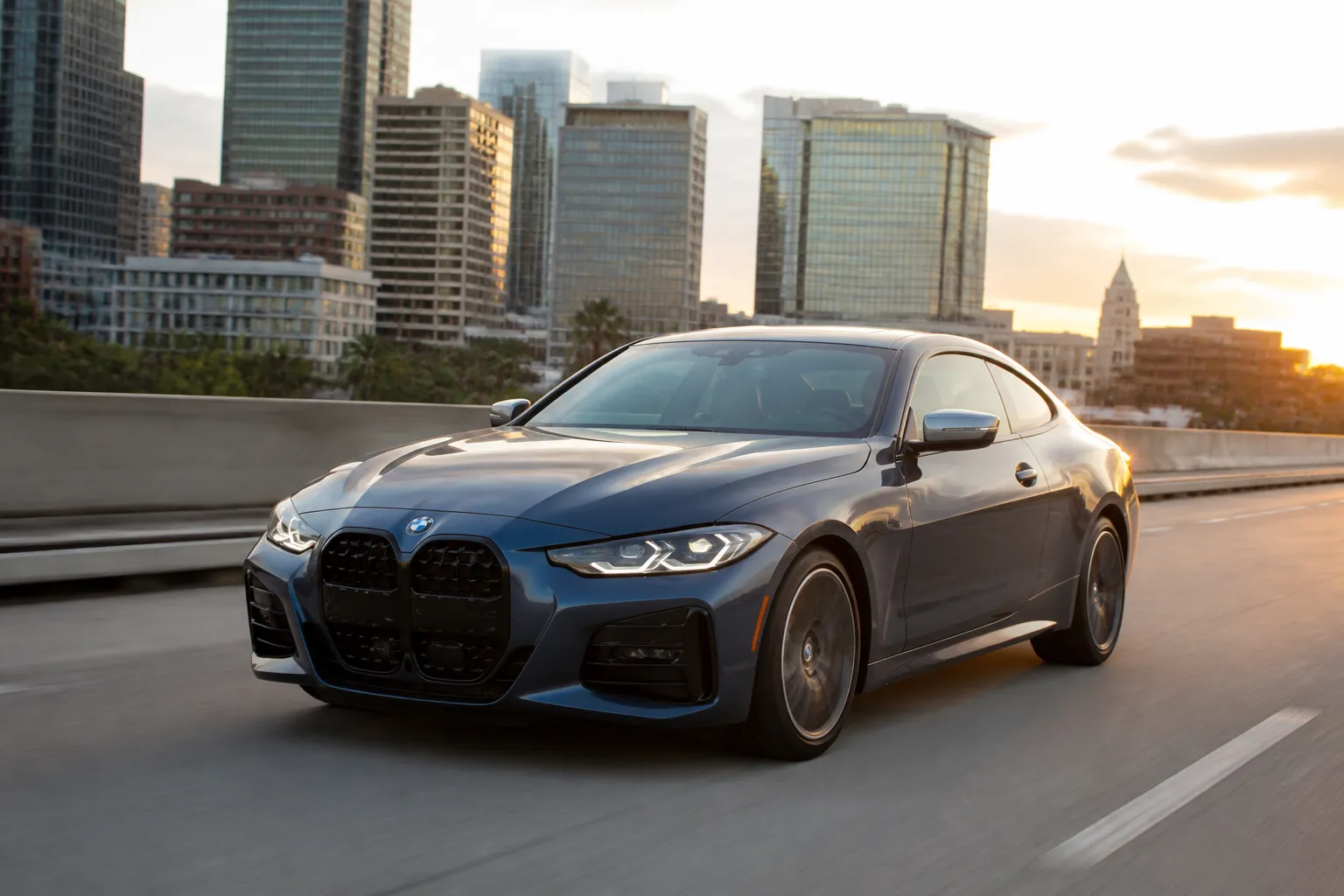 BMW 4-Series на городской дороге в вечернем свете. Автомобиль показан спереди под углом, акцент на кузове и дорожной обстановке.