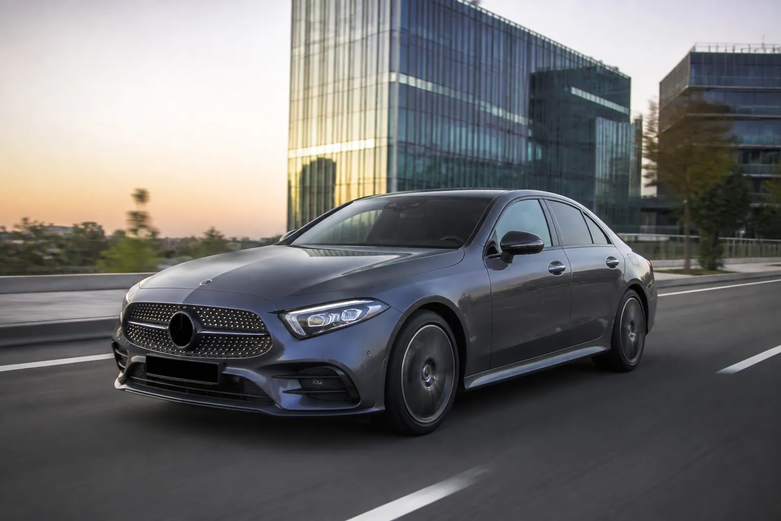Mercedes-Benz CLS-Class на городской дороге в вечернем свете. Автомобиль показан спереди сбоку, акцент на силуэте четырёхдверного купе.