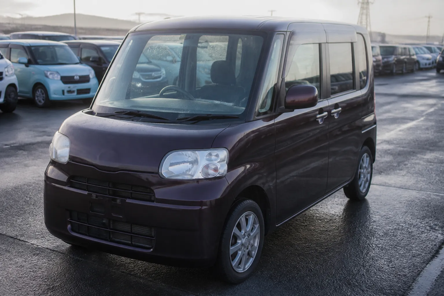 На обложке компактный японский кей-кар на площадке автомобильного аукциона. Машина стоит среди других автомобилей, подчёркивая тему покупки Daihatsu Tanto из Японии под ключ.