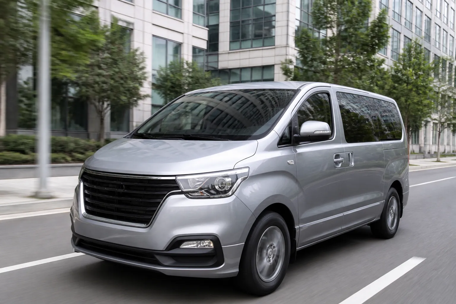 Hyundai Starex на городской дороге, снятый спереди под углом. Большой минивэн показан в повседневной среде, чтобы подчеркнуть семейный и пассажирский формат автомобиля.