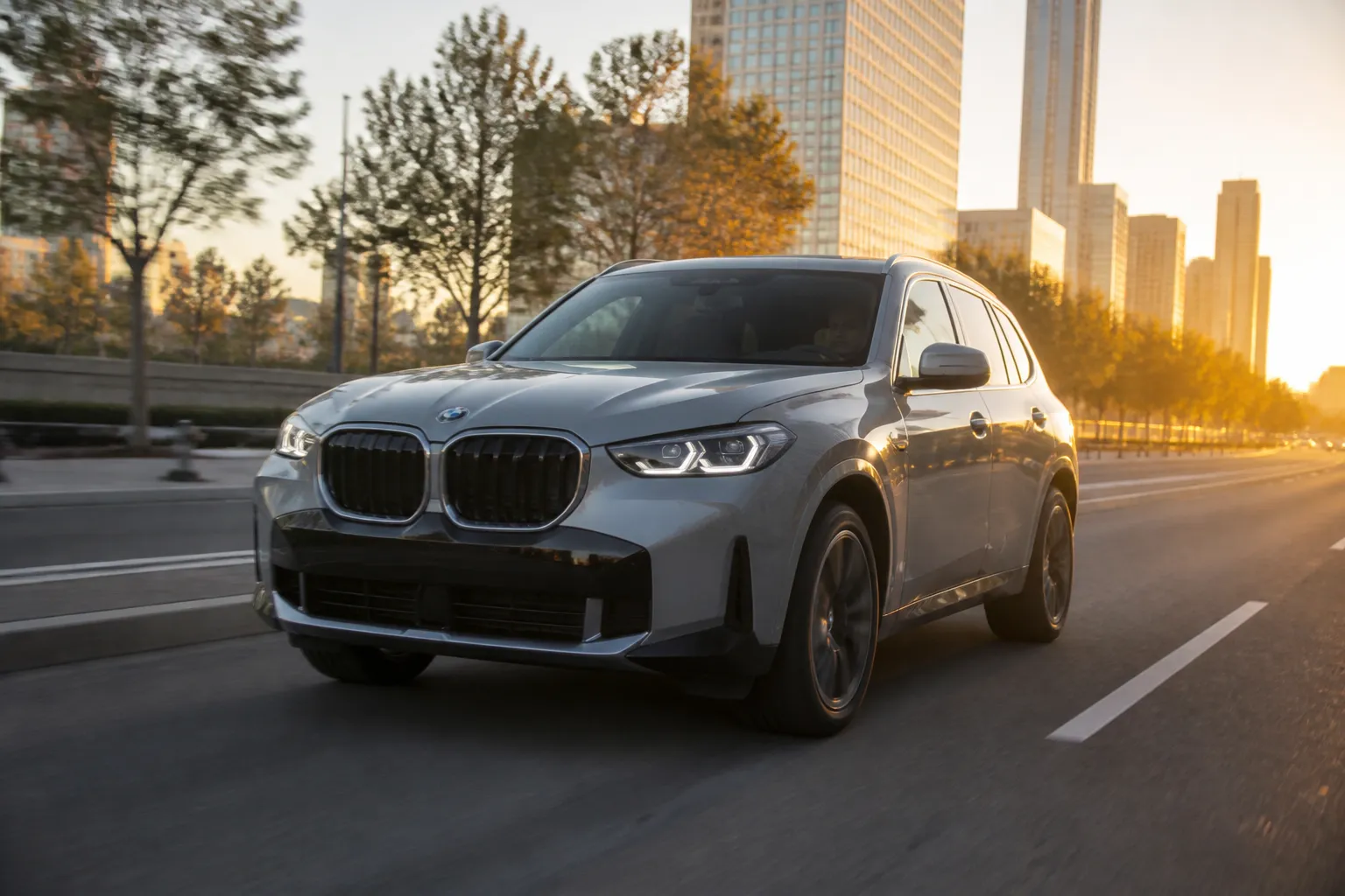 BMW X3 на городской дороге в вечернем свете, вид спереди под углом. На фоне современная улица и мягкое освещение без лишних деталей.
