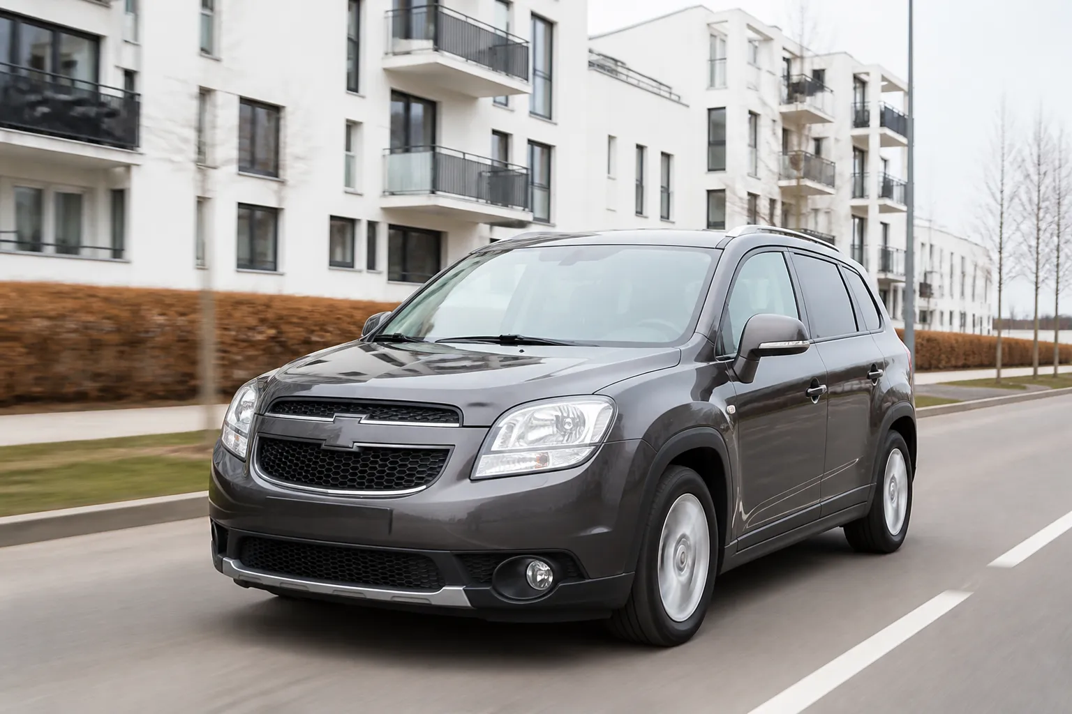 Chevrolet Orlando на городской дороге рядом с семейным кварталом. Автомобиль показан в естественном дневном свете, акцент на практичный кузов и повседневную эксплуатацию.